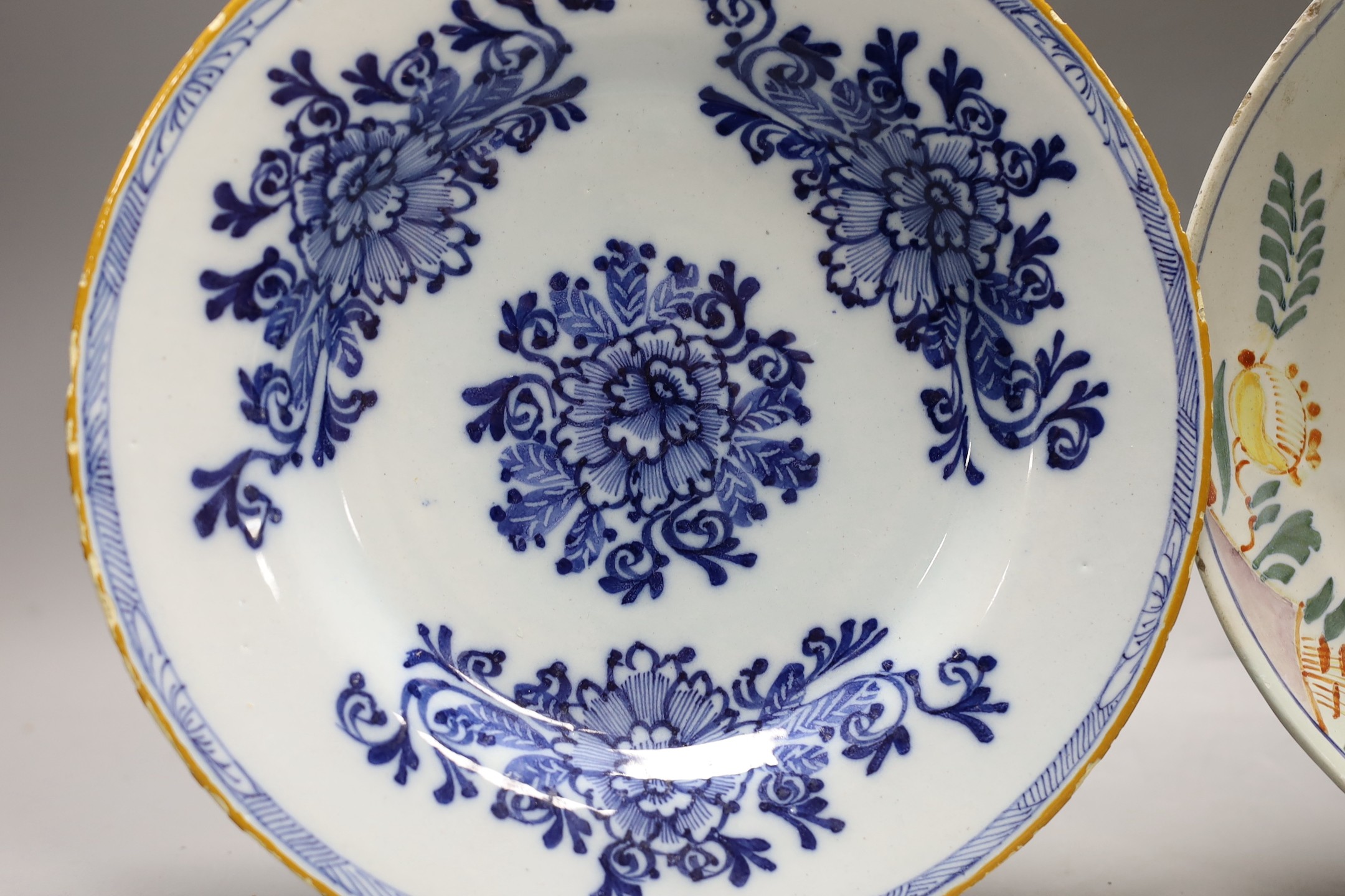 An early 18th century Delft polychrome dish and a mid 18th century Delft blue and white plate, largest 23.5cm diameter